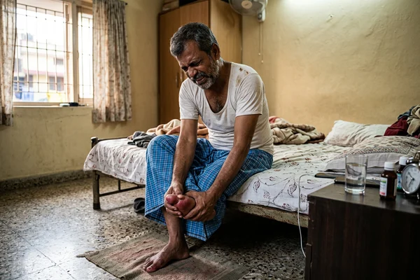 Indian man gripping swollen toe in acute gout pain